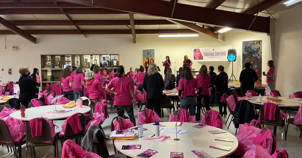Mentor in pink shirt welcoming hundreds of girls to the Girls on Fire Confidence Conference in a large community hall