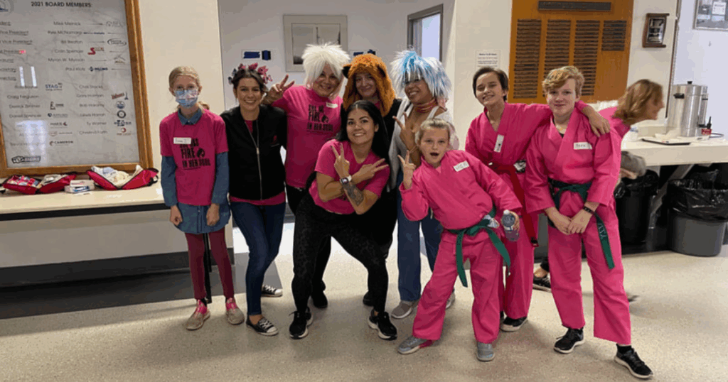 Girls on Fire mentors and participants in playful wigs and martial arts uniforms smiling and posing during confidence-conference event