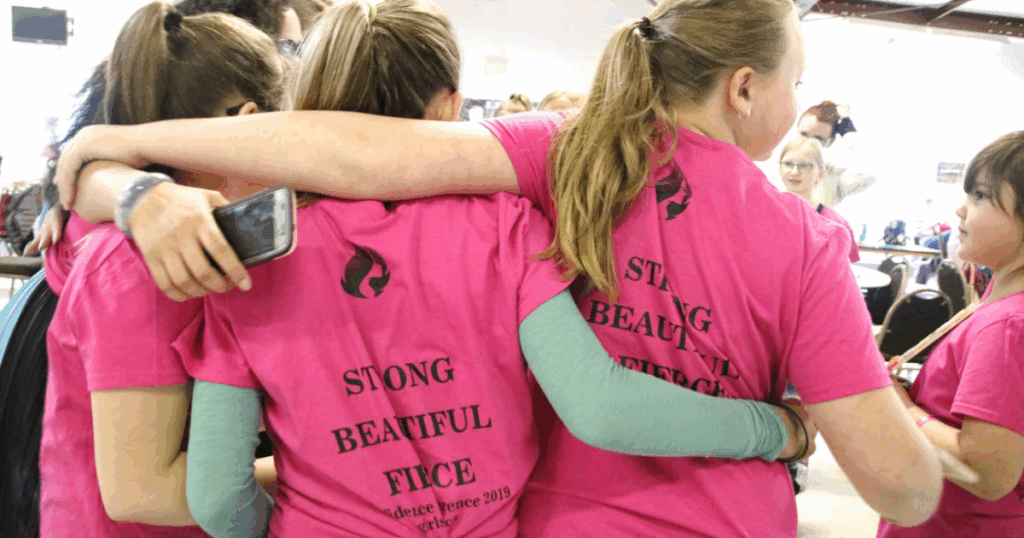 Girls hugging in matching Girls on Fire shirts with “Strong, Beautiful, Fierce” printed on the back during conference for mentorship for young girls
