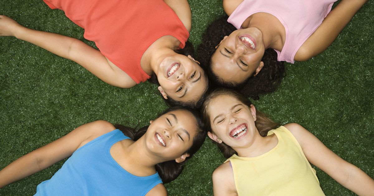 Tween girls smiling together on grass, building confidence, friendship, and self-love through Girls on Fire empowerment programs in Alberta