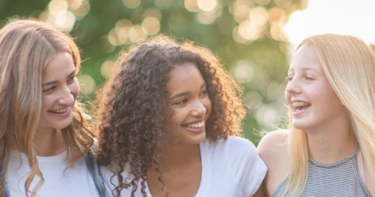 Preteen girls smiling together outdoors while building friendship and confidence during a girls-only leadership program.