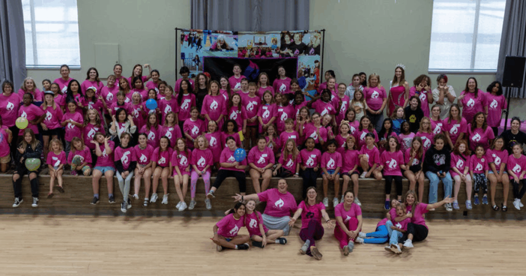 Large group of girls and women in bright pink Girls On Fire shirts gathered at an empowerment conference in Alberta, celebrating confidence, community, and youth mentorship.