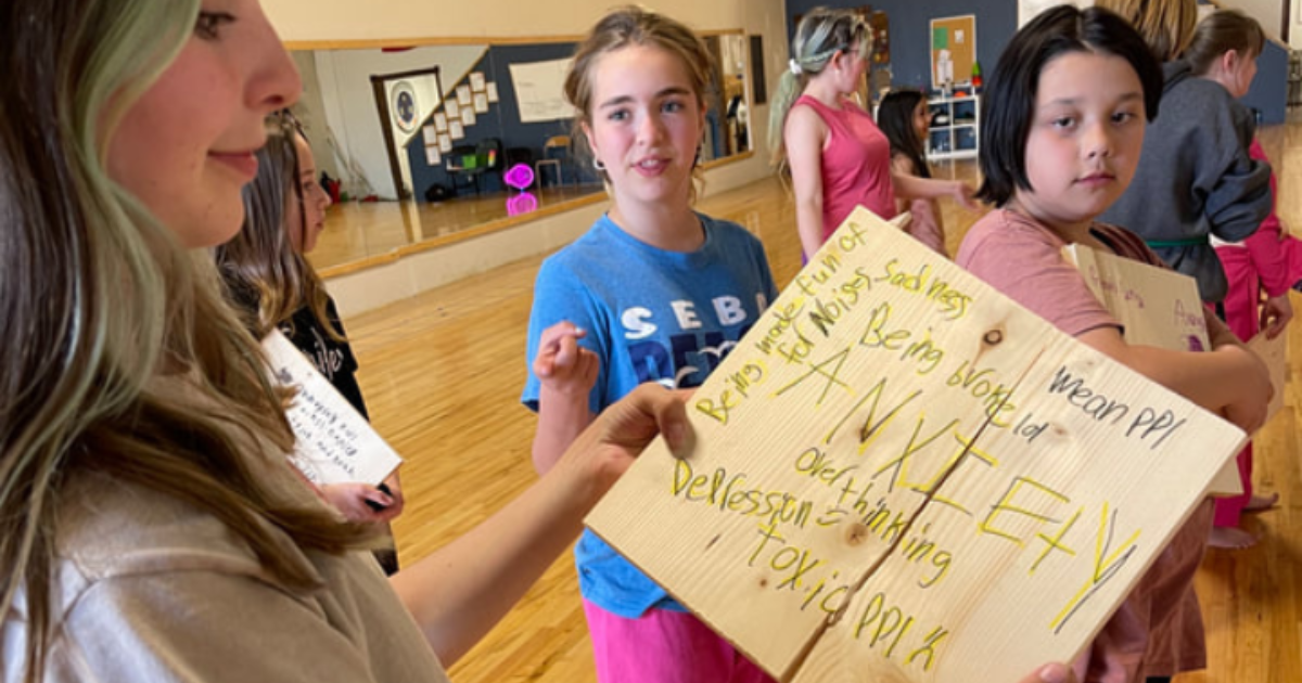 Girl in an Alberta youth leadership program that holds an “anti-bullying” poster during a confidence and mindset activity for ages 8–13.